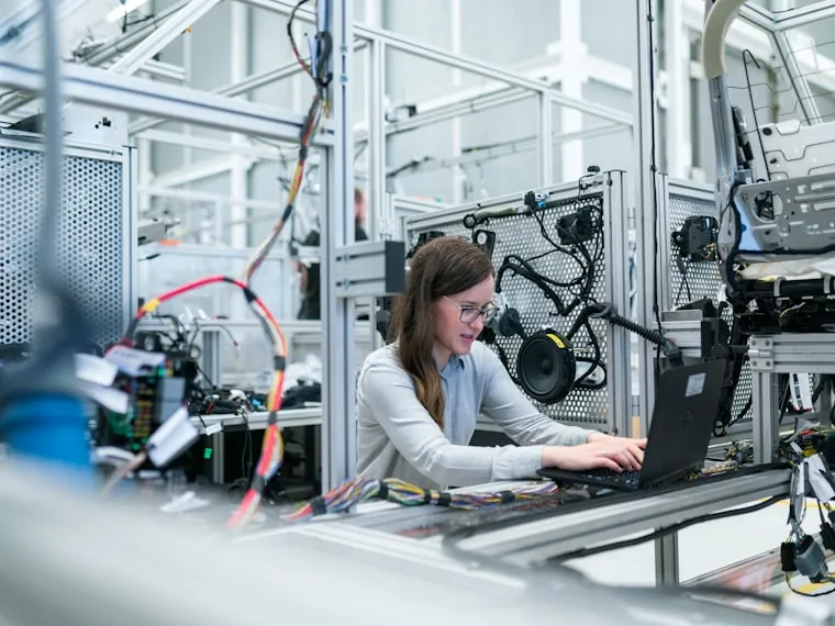 Ingeniera revisando una línea de producción automatizada con su computadora